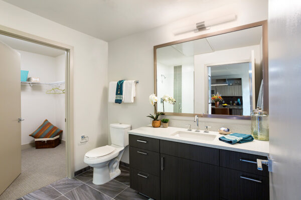 Bathroom with tile floor, wood cabinets, white counter, large mirror, and door to closet.