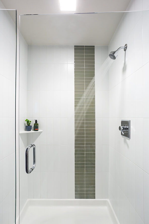 Tiled shower with glass door and corner shelf.