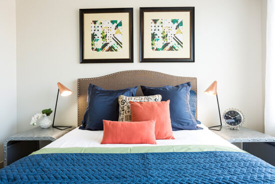 Bedroom with large platform bed, plush bedding, metal bedside tables, and geometric artwork.