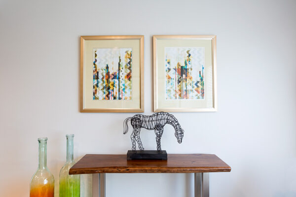 Detail of modern wood side table with wire horse sculpture and framed geometric artwork.