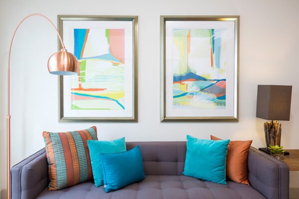 Living room with plush couch, colorful pillows, floor standing lamp, and framed artwork.