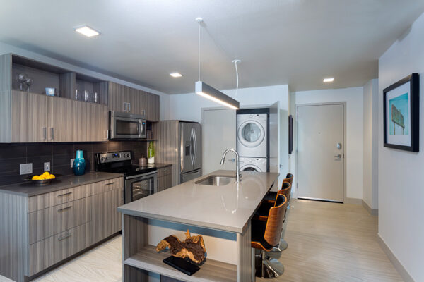 Kitchen with wood floor and cabinets, stone counters, stainless steel appliances, and island with stools.