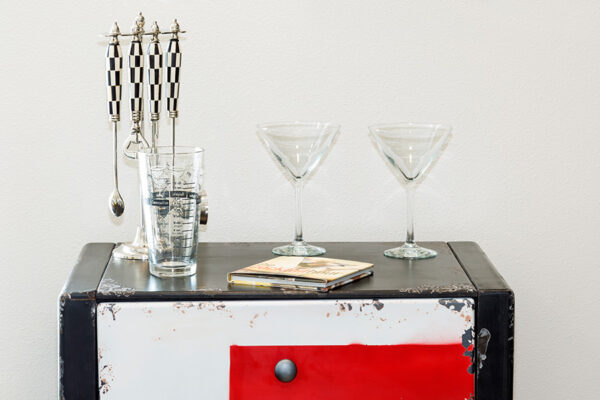 Detail of vintage cupboard topped with martini glasses and cocktail mixing tools.