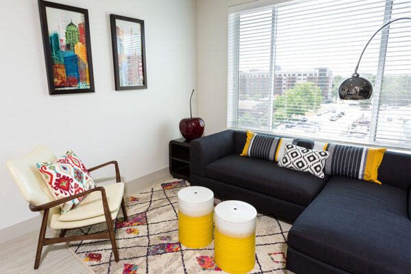 Studio living room with plush sectional, modern chair, floor standing lamp, and large window.