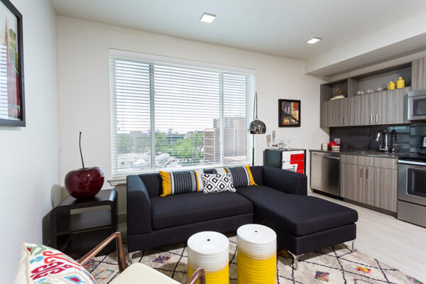 Studio living space with kitchen, large plush sectional, and large window.