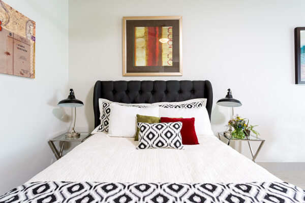 Detail of studio living area with platform bed, glass and metal bedside tables, and artwork.