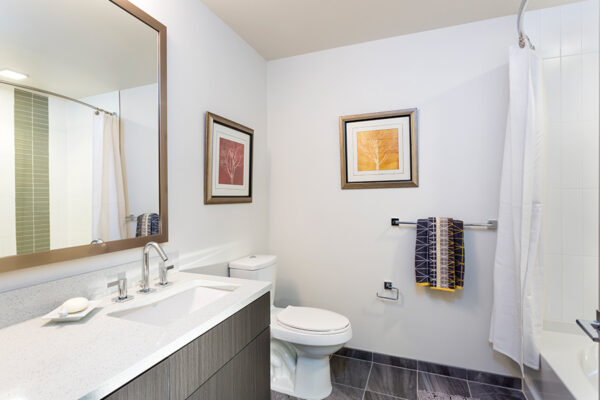 Bathroom with tile floor, wood cabinet, white counter, and large framed mirror.