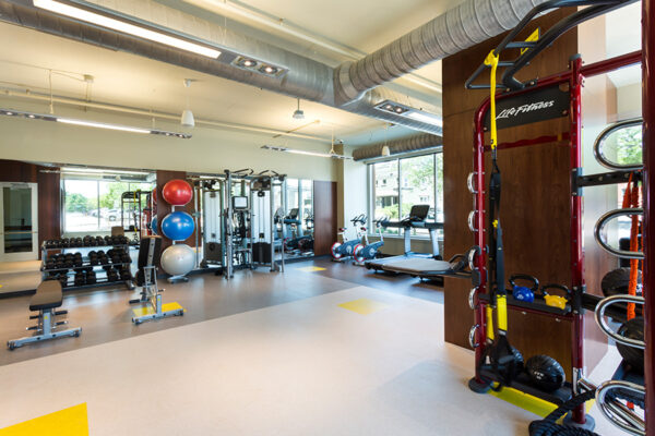 Fitness center with cardio and weight equipment, mirror walls, and large windows.