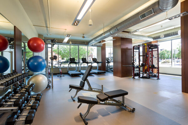 Fitness center with cardio and weight equipment, mirror walls, and large windows.