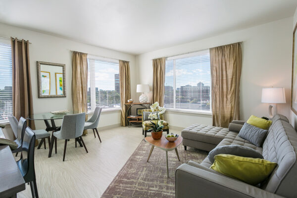 Apartment living space with wood floor, large rug, plush sectional couch, dining table, and large windows.