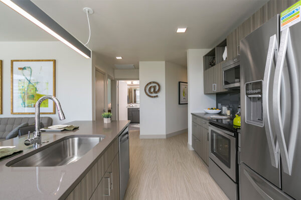 Kitchen with wood floor and cabinets, stone counters, stainless steel appliances, and hallway to other rooms.