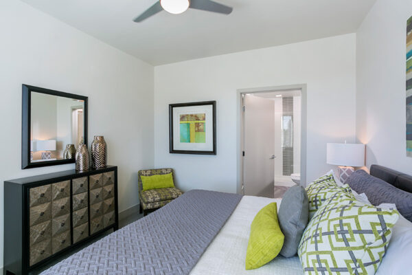 Bedroom with large plush bed, chic dresser, large framed mirror, and door to bathroom.