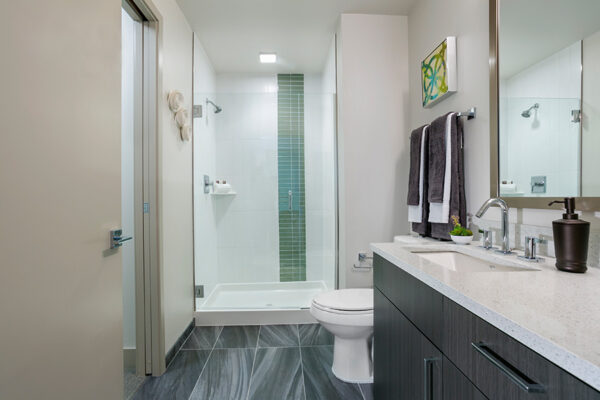 Bathroom with tile floor, wood cabinets, stone counter, and tiled shower with glass door.