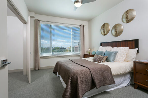 Bedroom with carpet, large platform bed, wood furniture, and large window.