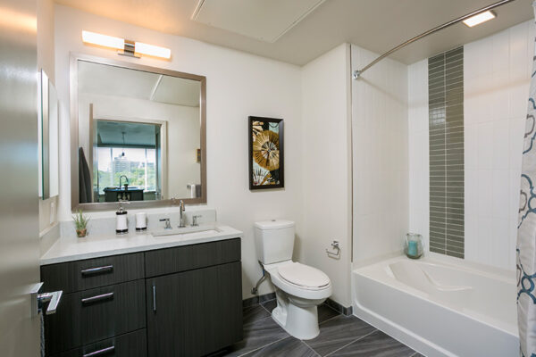 Bathroom with tile floor, wood cabinet, white counter, large mirror, and tiled shower tub.