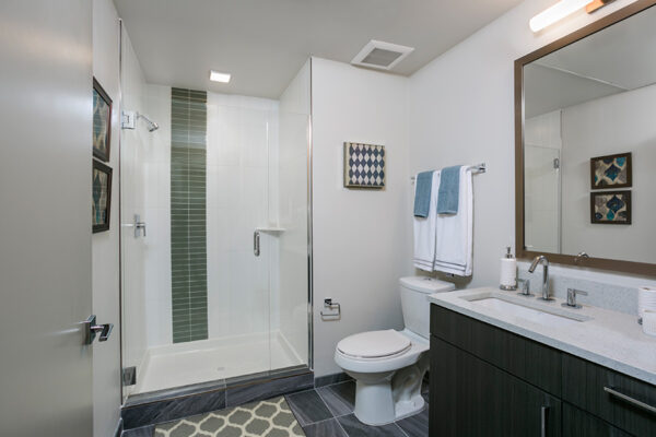 Bathroom with tile floor, wood cabinet, large framed mirror, and tiled shower with glass door.