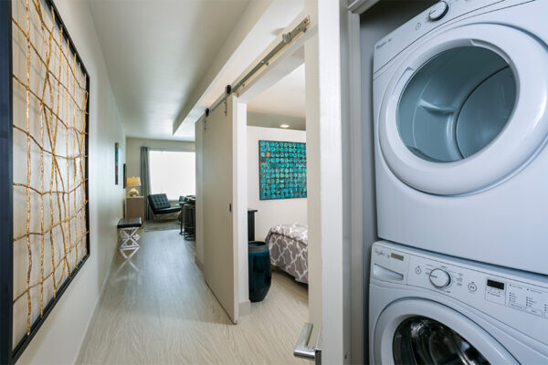 Apartment hallway with laundry closet, entrance to bedroom, and hallway to living space.