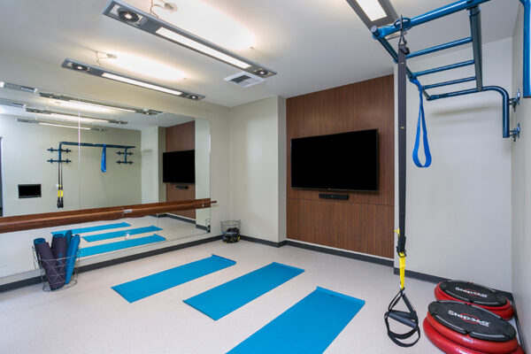 Fitness room with yoga mats, mirrored wall, and large TV.