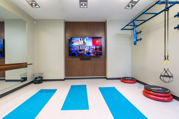 Fitness room with yoga mats, mirrored wall, and large TV.