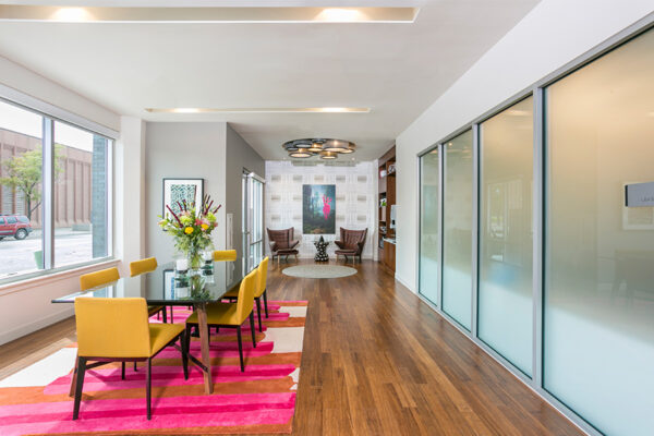 Lounge area with wood floor, colorful rug and chairs, and large frosted glass walls.