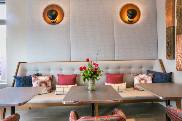 Lounge with booth seats and tables, padded wall, and modern sconce lights.