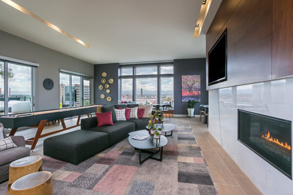Lounge with rug, large sectional couch, fireplace, wall mounted TV, and shuffleboard table.