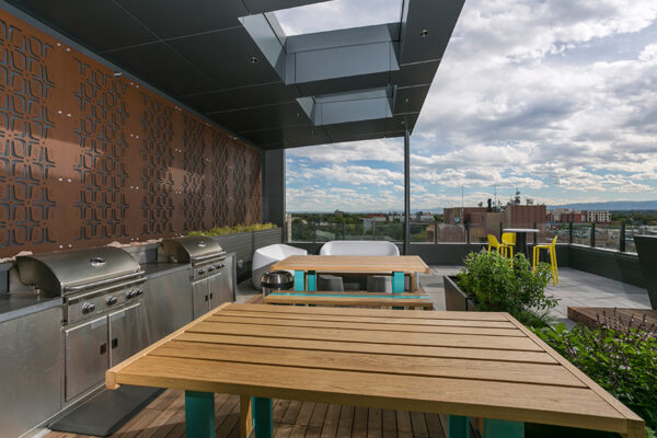 Rooftop patio with tall picnic tables and built in BBQ grills overlooking Denver.