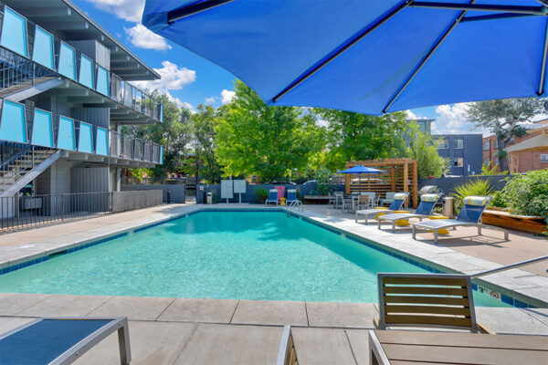 Pool area with lounge chairs and tables overlooked by apartment balconies.