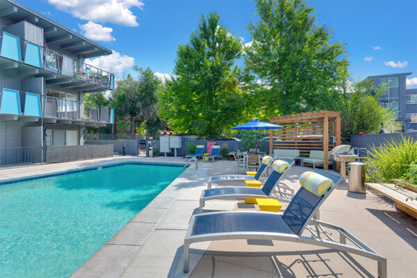 Pool area with lounge chairs and tables overlooked by apartment balconies.