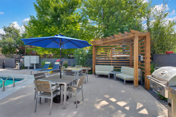 Pool area with lounge chairs, tables, umbrellas, and wood pergola.