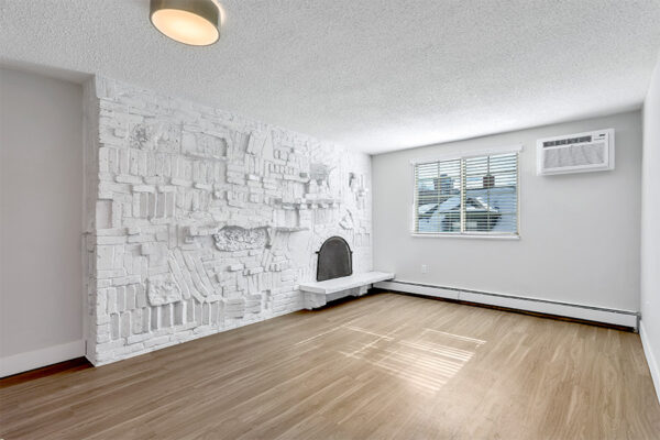 Living room with wood floor, baseboard heater, white brick accent wall with fireplace, and large window.