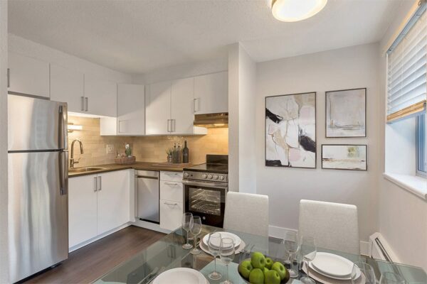 Apartment kitchen with wood floor, white cabinets, and stainless steel appliances.