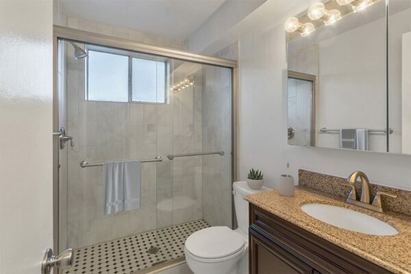 Bathroom with wood cabinet, stone counter, and glass shower.