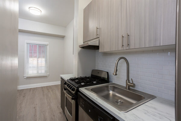 Kitchen with wood floor, dark cabinets, light counters, tiled backsplash and stainless steel appliances.