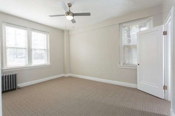 Bedroom with carpet, warm gray walls, white trim, ceiling fan, and large windows.