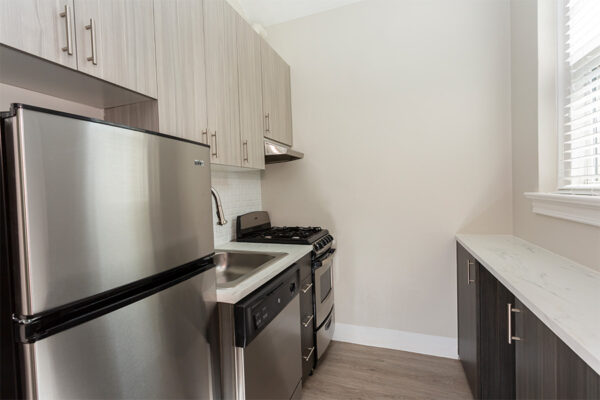 Kitchen with wood floor, dark cabinets, light counters, and stainless steel appliances.