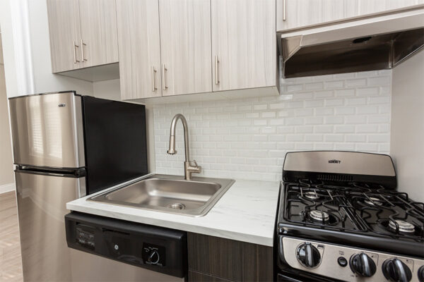 Kitchen with dark cabinets, light counters, stainless steel appliances, and tiled backsplash.