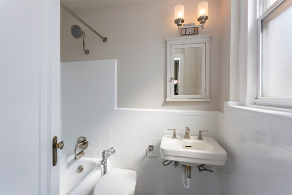 Bathroom with tiled shower tub, medicine cabinet, and large frosted window.