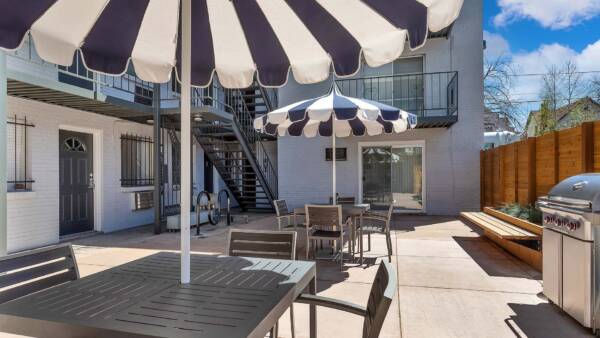 Patio with dining tables and BBQ grill overlooked by apartment balconies.