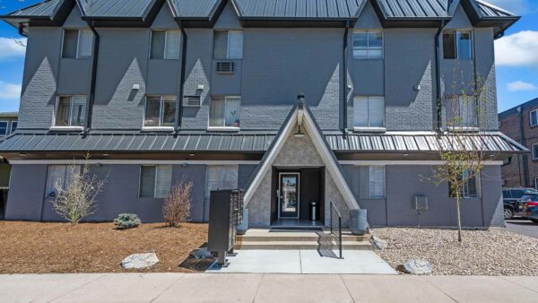 960 Logan apartment building with grey bricks, rocky landscaping, and mature trees.