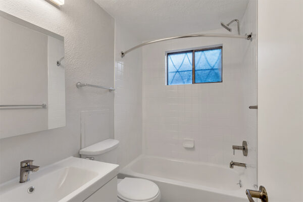 Bathroom with tiled shower tub, white cabinet, white counter, and medicine cabinet.