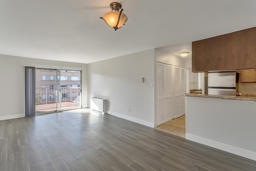 Living room with wood floors, cool gray walls, entry to kitchen, and door to balcony.