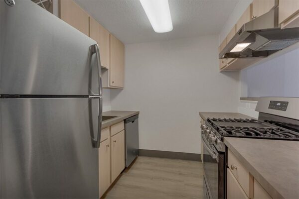 Kitchen with wood floor and cabinets, tan counters, and stainless steel appliances.