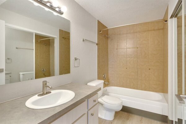 Bathroom with wood floor and cabinet, tan counter, large mirror, and tiled shower tub.