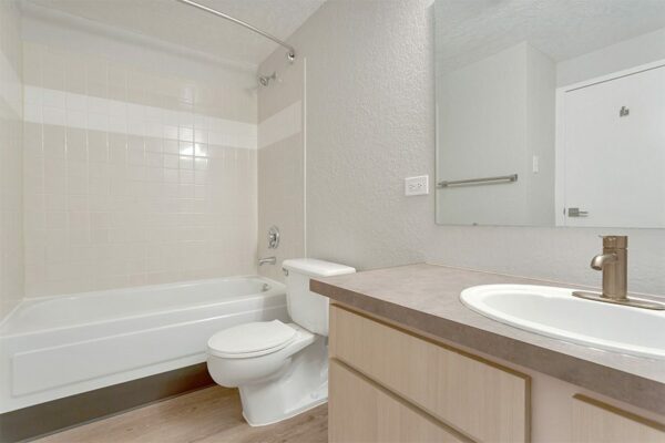 Bathroom with wood cabinets, tan counters, large mirror, and tiled shower tub.