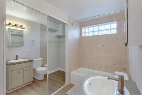Bathroom with wood floor and cabinet, closet with mirror door, and tiled shower tub.