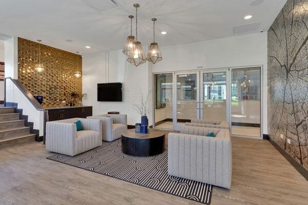 Lounge with wood floor, plush chairs, wall mural of tree, gold tile accent wall, and decorative lighting fixtures.