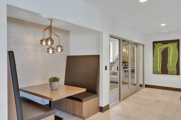 Booth with plush seats, wood table, potted succulent, and modern decorative lighting fixture near glass entry doors.