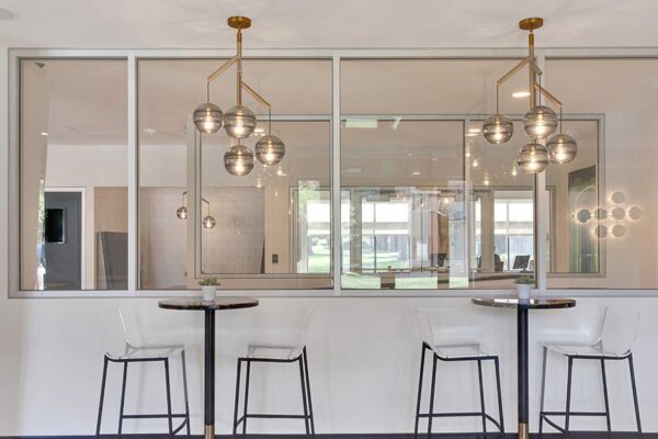 Game room with bar tables with stools, decorative modern lighting fixtures, and glass wall.