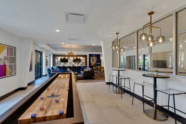 Game room with tile floor, bar tables with stools, decorative modern lighting fixtures, and shuffleboard table.